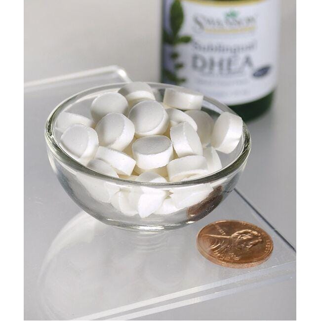 A bowl of white pills next to a bottle of Swanson DHEA - 25 mg 60 lozenges Cherry Flavor.