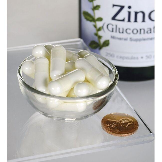 A bottle of Swanson Zinc Gluconate - 50 mg 250 capsules and a penny on a table.