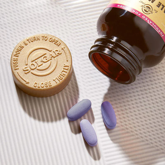 A brown bottle of Solgar Female Multiple 60 Tablets rests open on a surface beside its cap, with three purple tablets spilled out.