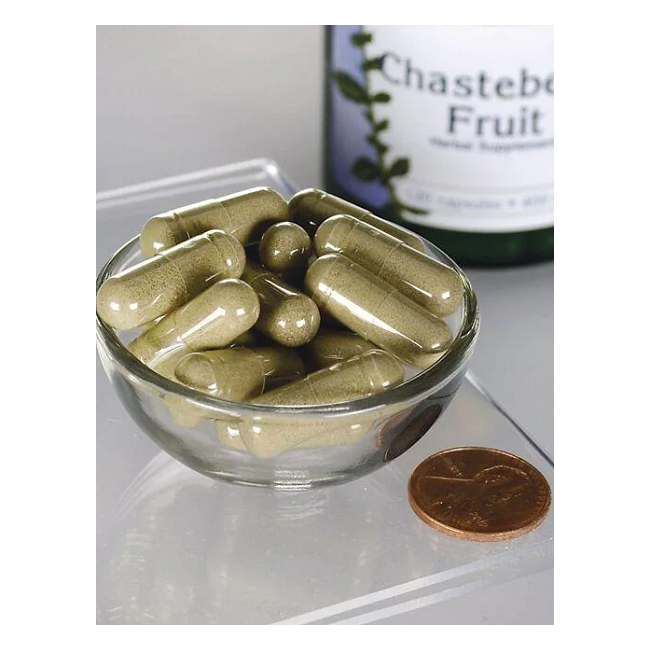 A small Swanson Chasteberry Fruit 400 mg capsule bottle is partially visible behind a glass bowl of green capsules, placed next to a penny for scale, showcasing their modest size and highlighting their role in supporting women's health and menstrual cycle regulation.