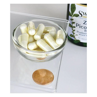 Thumbnail for A small glass bowl of white capsules sits on a clear surface beside a penny for scale. Part of a Swanson supplement bottle labeled in green and yellow is visible in the background, suggesting its Zinc Picolinate 22 mg content, known for supporting the immune system.