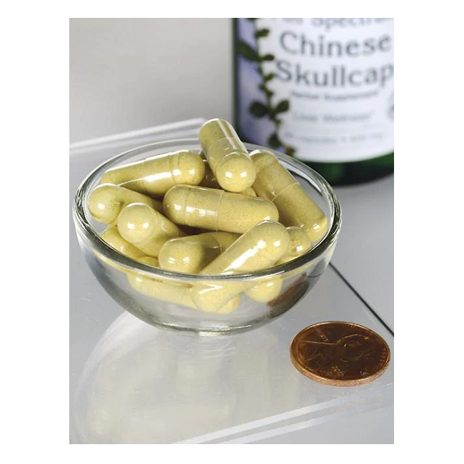 A glass bowl of yellow capsules sits beside a penny for scale, with a bottle labeled "Swanson Chinese Skullcap 400 mg 90 Capsules," highlighting the product's roots in traditional Chinese herbal medicine.