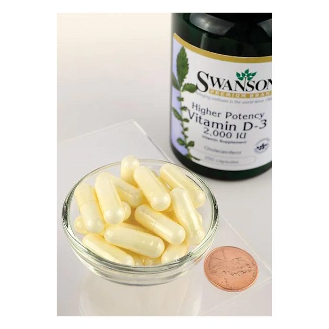 A bowl of yellow capsules is next to a Swanson Vitamin D3 2000 IU 250 Capsules bottle and a penny for scale, emphasizing the role of Vitamin D3 in supporting bone health.