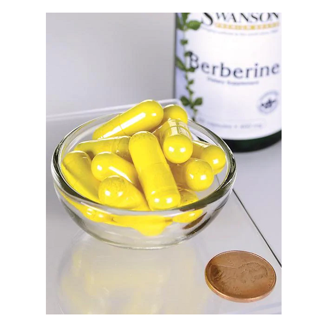 A small glass bowl holds yellow capsules beside a penny for scale, highlighting their size. In the background is a bottle labeled "Swanson Berberine - 400 mg 60 capsules," known for enhancing blood sugar metabolism and cardiovascular health.