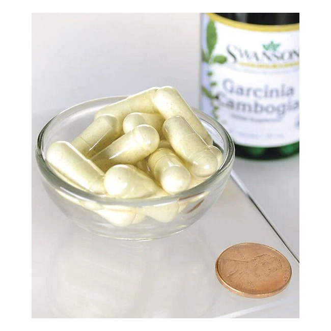 A small glass bowl contains several white capsules beside a coin for scale. In the background, a partially visible Swanson Garcinia Cambogia 5:1 Extract bottle suggests its hydroxycitric acid content for effective weight management.