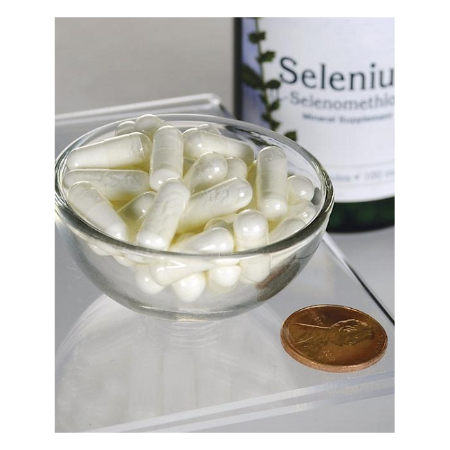 A bowl of white capsules sits beside a US penny for scale, with a Swanson Selenium L-Selenomethionine 100 mcg 200 Capsules bottle in the background, emphasizing its immune support and enhanced bioavailability.