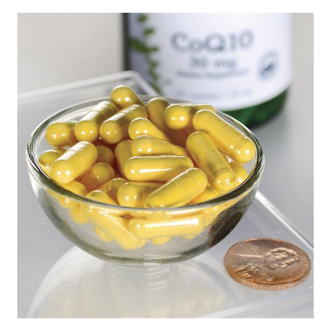 A glass bowl with yellow capsules shines on a reflective surface next to a penny for scale, with a bottle of Swanson Coenzyme Q10 30 mg 120 Capsules in the background. These capsules are essential for energy production and cardiovascular health.