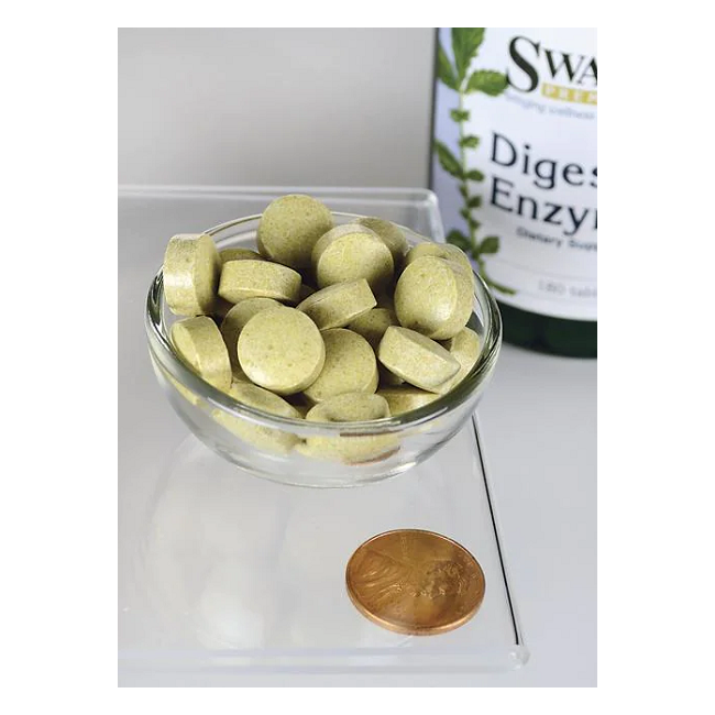 A small glass bowl filled with green tablets sits beside a penny for scale, next to a partly visible Swanson bottle labeled "Digestive Enzymes 180 Tablets," suggesting their role in promoting healthy digestion.