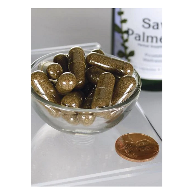 Next to a penny, a small glass bowl with brown capsules appears beside a Swanson Full Spectrum Saw Palmetto 540 mg bottle, suggesting benefits for prostate health and DHT regulation.