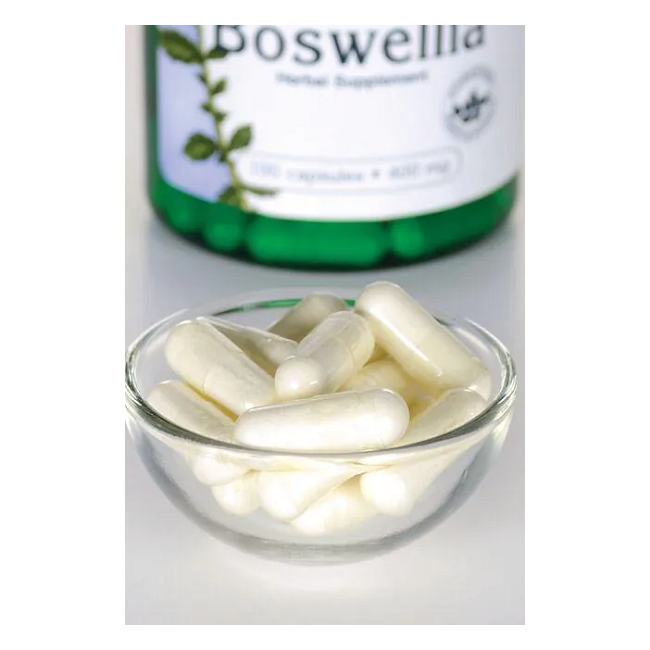 A glass bowl filled with white capsules sits in front of a blurred bottle of Swanson Boswellia 400 mg, known for supporting joint health.