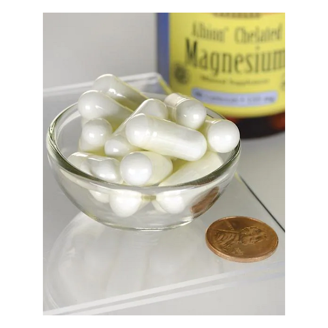 A small glass bowl filled with white capsules is next to a penny. In the background, a bottle labeled "Swanson Albion Chelated Magnesium Glycinate 133 mg 90 Capsules" indicates it supports muscle health.