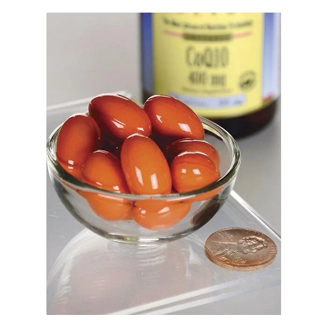 A small glass bowl filled with glossy red capsules, shown next to a penny for scale, sits in front of Swanson Coenzyme Q10 400 mg 30 Softgels bottle, emphasizing its benefits for energy production and cardiovascular health.