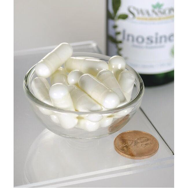 A bowl of white pills next to a bottle of Swanson Inosine - 500 mg 60 vege capsules.