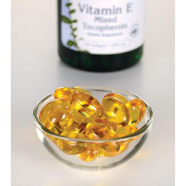 Swanson Vitamin E - 400 IU 100 softgel Mixed Tocopherols, an antioxidant support and essential nutrient for cardiovascular health, displayed in a bowl alongside a bottle, is designed to combat free radical damage.