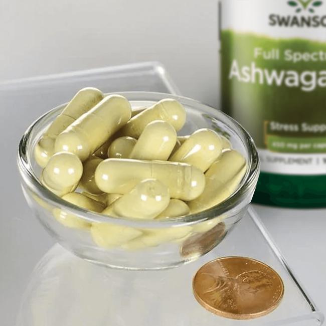 A bowl of Swanson Ashwagandha - 450 mg 100 capsules with a coin next to it.