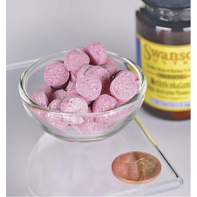 A glass bowl containing pink pills, including Swanson Vitamin B-12 - 5000 mcg 60 tabs Methylcobalamin supplements, placed next to a penny.
